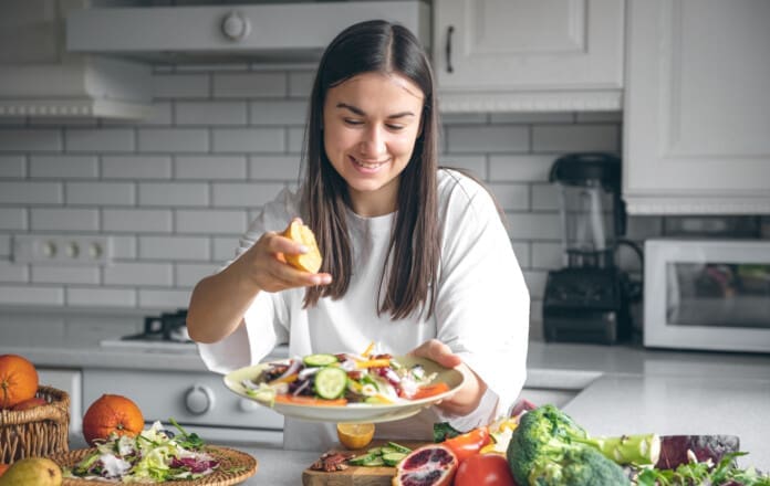 A woman makes a salad of fresh vegetables, squeezes the juice of a lemon.