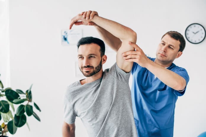 chiropractor stretching arm of handsome patient in hospital
