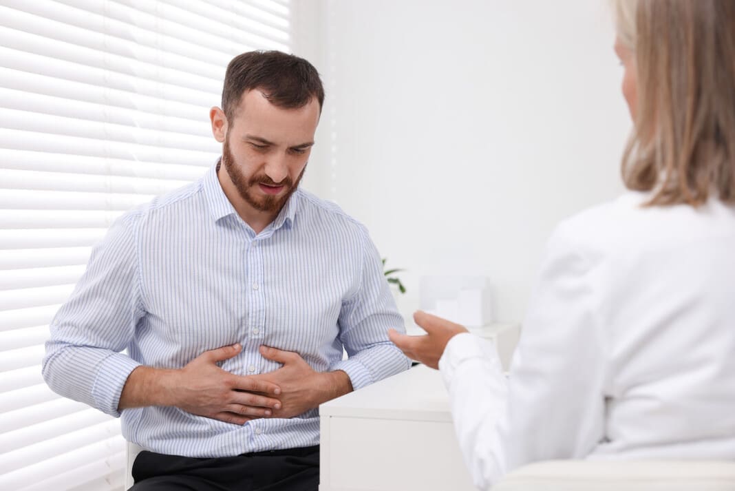 Doctor consulting patient with stomach pain at table in clinic,