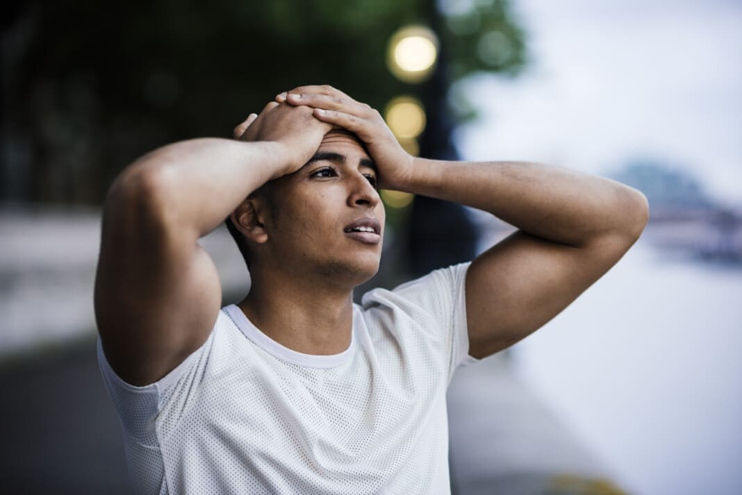 Male runner with hands on forehead taking a break on riverside