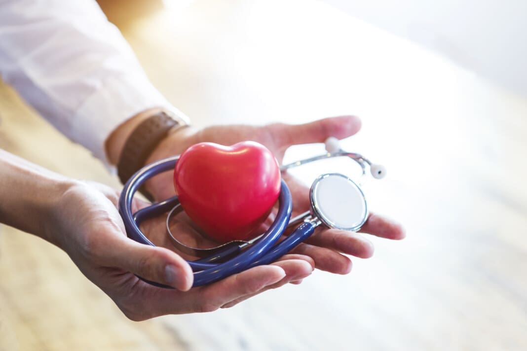 Doctor holding stethoscope and red heart on hands with white spa