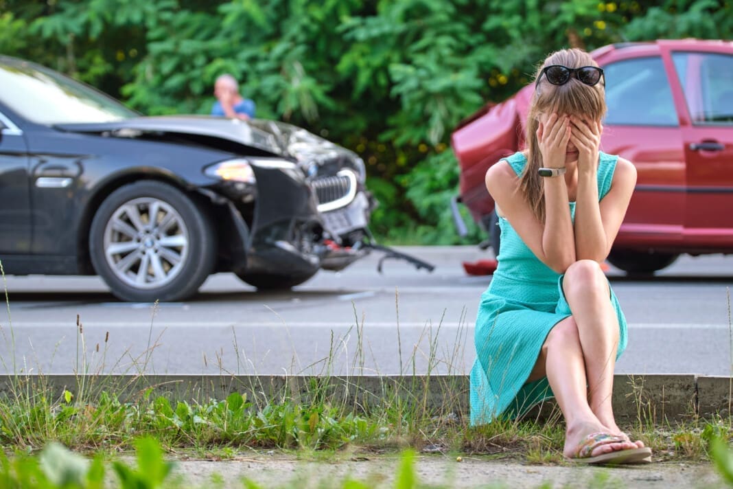 Sad female driver sitting on street side shocked after car accident. Road safety and vehicle insurance concept. Memorial Day Rear-End Accidents and Collisions Awareness