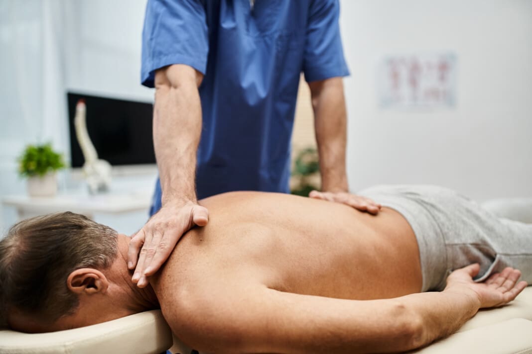 cropped view of devoted doctor in medical robe massaging his mature patient during rehabilitation